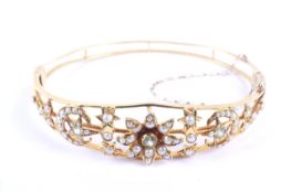An Edwardian gold, peridot and half-pearl openwork hinged bangle.