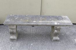 A reconstituted stone garden bench. The bench ends of scrolling form, decorated with vines.