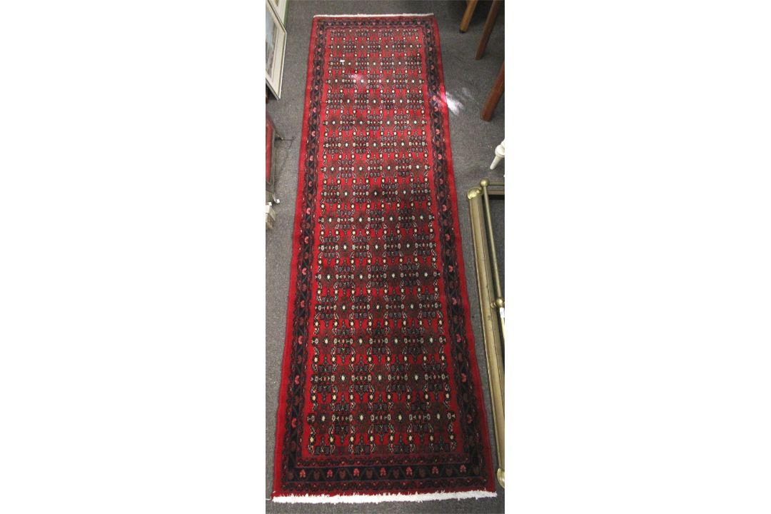 A Persian style red ground wool runner carpet. With a dark blue border and geometric pattern.
