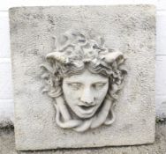 A weathered concrete wall mounted Medusa mask.
