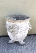 A weathered reconstituted stone garden urn on three lion's paw feet.