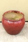 A large round red glazed garden pot/jardiniere.