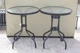A pair of black metal and glass round garden tables.
