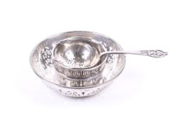 A silver tea strainer and bowl and a round sweet dish.