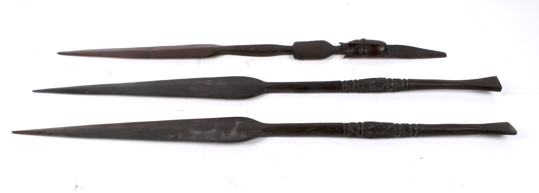 Three African wood spear heads. One carved with a head, the other with rows of lines. Largest L74cm.
