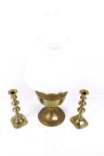 A brass oil lamp and two brass candlesticks. The lamp with a white glass shade.