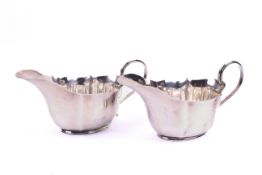 A pair of shaped silver milk jugs. With reeded handle and four-section body over a short foot.
