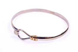 A hallmarked 9ct white gold bangle. With tension clip fitting and yellow gold details.