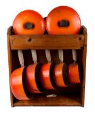 A graduated set of five vintage Le Creuset orange enamel saucepans and lids. In a pine stand. No.