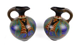 A pair of Gouda jugs. Decorated with red and blue patterned decoration, one damaged, H27cm.