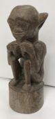 A 1950s Malaysian carved teak figure of a large eared gentleman seated pulling on his beard upon a