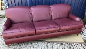A modern burgundy leather upholstered three seat sofa in the manner of Howard of London on turned