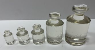 A graduated set of five moulded glass cylindrical weights, possibly shop display examples,