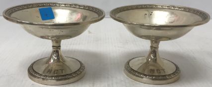 A pair of white metal pedestal dishes with scrolling decoration,