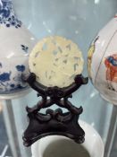 A 20th century carved white jade pendant on carved wood stand, pendant 50mm diameter, height of