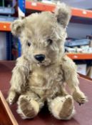 A vintage teddy bear with articulated arms and legs, brown eyes (presumed glass) and black nose.