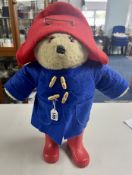 A bear dressed with a red hat, red wellies and a blue felt coat.