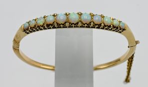 A 9ct yellow gold bangle, set with eleven graduated opals set between diamond chips (diameter