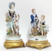 Two German Sitzendorf style figurines, depicting a girl and boy and girl and dog, on gilt stands. (