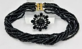 A nine-strand jet necklace, with jet inlaid metal clasp, together with a jet flower brooch (
