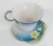 A Franz teacup and saucer, green raised leaf and flower pattern on a blue and white ground.
