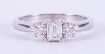 A platinum three stone ring set with a central emerald cut diamond, approx. 0.40 carats, with a