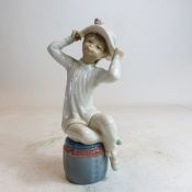 Lladro figure of seated child trying on hat, h.22cm.