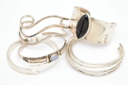 FIVE WHITE METAL BANGLES, the first a wide white metal cuff bangle, set with a navette cabochon