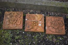 THREE WEATHERED COMPOSITE TILES, each with a different pattern of a flower head, 30cm squared (