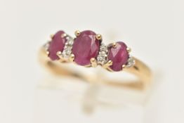 A 9CT GOLD RUBY AND DIAMOND RING, designed with a row of three oval cut rubies, each in a four