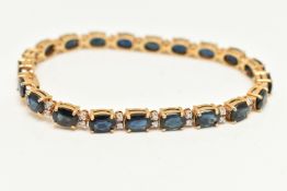 A YELLOW METAL SAPPHIRE AND DIAMOND LINE BRACELET, designed with a row of twenty one oval cut blue