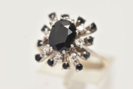 A WHITE METAL DRESS RING, designed as a square cluster ring, set with a central oval cut deep blue