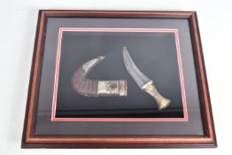 A FRAMED MIDDLE EASTERN STYLE JAMBIYA KNIFE, this has a decorative handle and a curved scabbard,