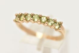 A 9CT GOLD SEVEN STONE RING, set with seven circular cut green stones believed to be peridot, each