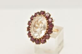 A YELLOW METAL ROCK CRYSTAL AND GARNET CLUSTER RING, set with an oval shape rock crystal,