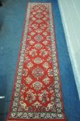 A RED GROUND RECTANGULAR CARPET RUNNER, with repeating patterns, surrounded by a multi-strap border,