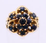 An unmarked gold and sapphire flowerhead ring. Ring size N/O.