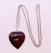 An amber heart shaped pendant on a silver chain, the former 3 cm high.