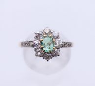 An unmarked gold diamond and emerald flowerhead ring. Ring size L/M.