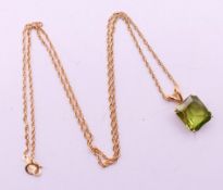 A gold and green stone, possibly peridot, pendant on a 14 K gold chain. The pendant 1.5 cm high.