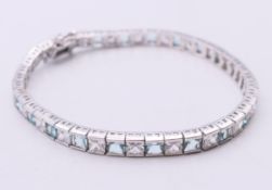 A silver tennis bracelet set with alternating clear and aqua coloured stones. 19 cm long.
