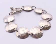 A silver bracelet with a hammered disc design. 20 cm long.