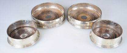 Two pairs of Elizabeth II feature hallmarked silver mounted wine bottle coasters, one pair London