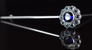 A white metal brooch set with a round cut synthetic sapphire surrounded by aquamarines, 4.6g, 6.8cm