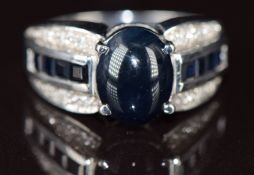 A 9k white gold ring set with a sapphire cabochon, calibre cut sapphires and diamonds, 5g, size N