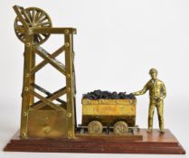 Novelty brass model of a coal miner with truck of coal beside a pit head gear, length 33cm