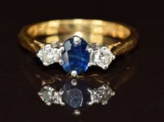 An 18ct gold ring set with an oval cut sapphire and two diamonds, 2.7g, size H