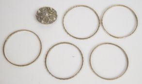 Five Libyan silver bangles with floral and circular decoration and a white metal brooch