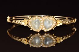 A c1900 9ct gold bangle set with heart shaped moonstones surrounded by seed pearls, with pierced and