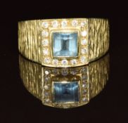 An 18k gold ring set with paste surrounded by diamonds, with textured shoulders, 6.4g, size Q